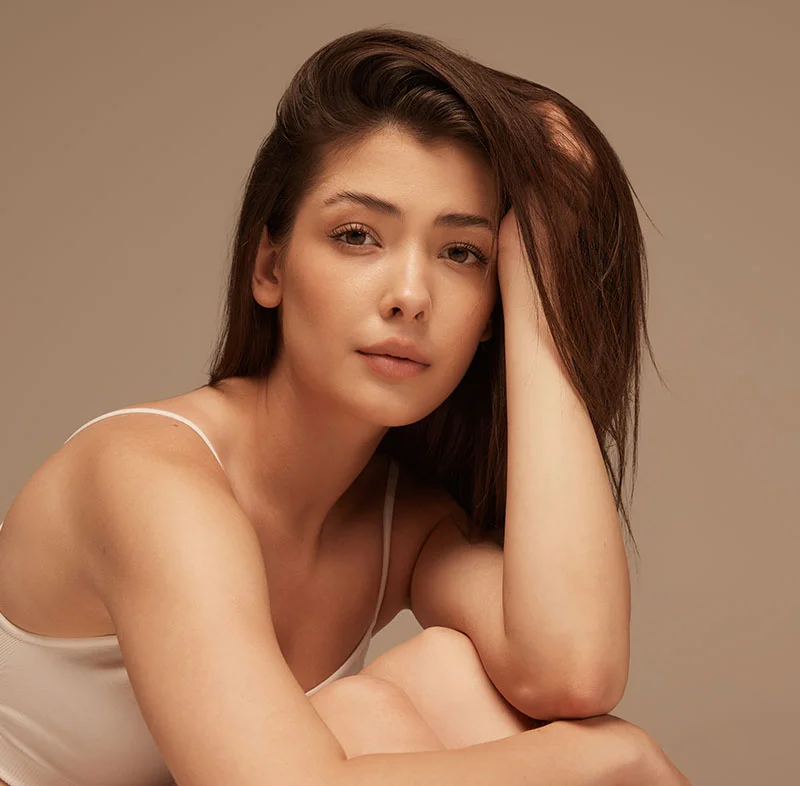 Woman with dark hair resting her head on one hand, looking thoughtful against a beige background - ClearSilk Laser Treatment in Red Bank, NJ