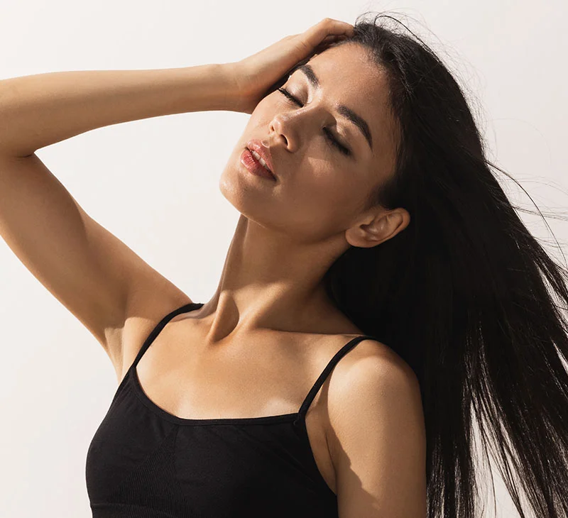 Woman with long, dark hair posing with her eyes closed, one hand resting on her head - Dermaplaning in Red Bank, NJ
