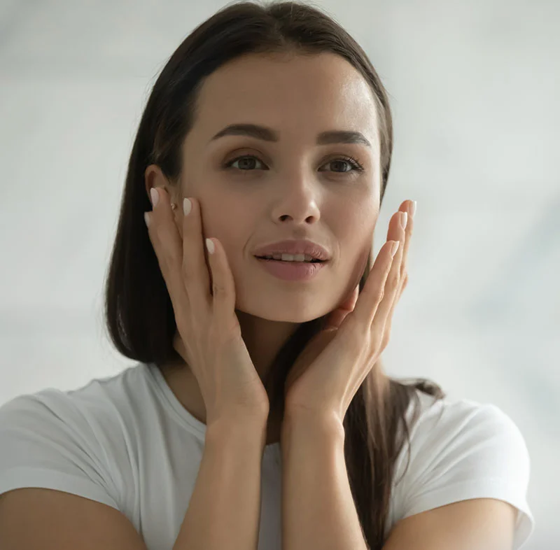 Woman with dark hair, gently touching her face - Facials in Red Bank, NJ