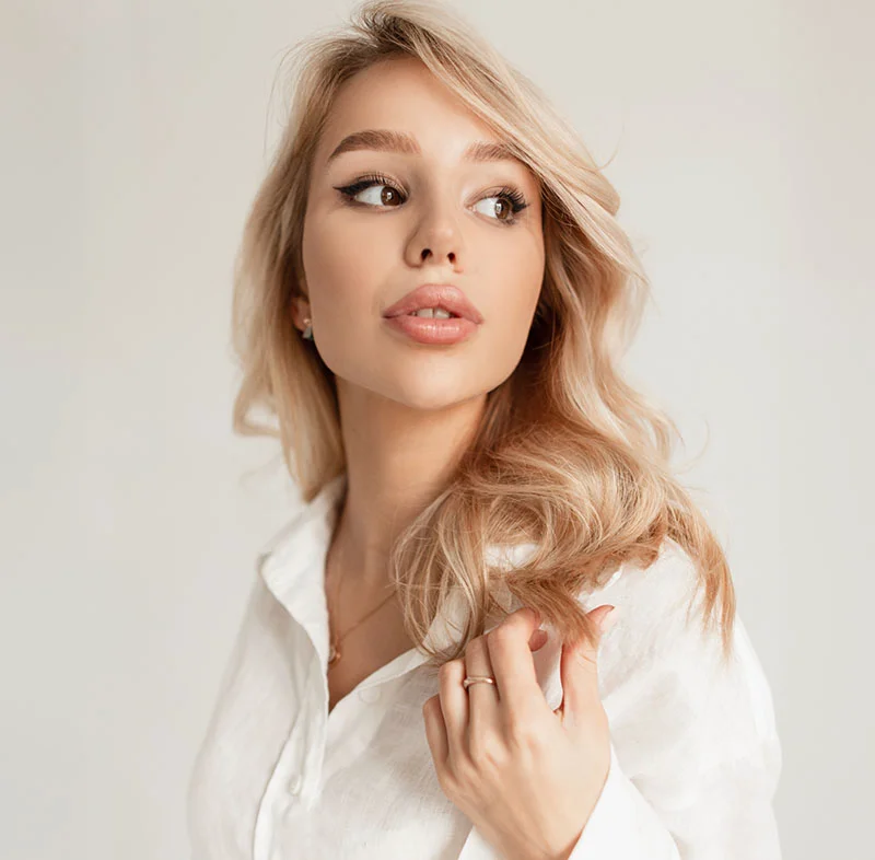 A woman with light blonde hair and bold eyeliner gazes off to the side, her hand lightly touching her hair - Hylenex in Red Bank, NJ