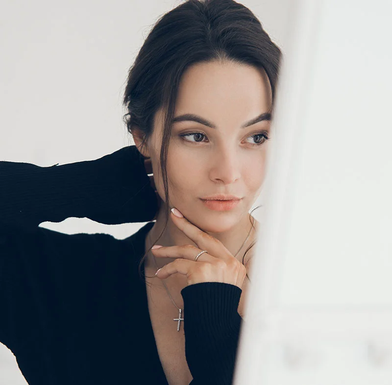 A woman with dark hair wearing a black top, posing with one hand beneath her chin - Liquid Rhinoplasty in Red Bank, NJ