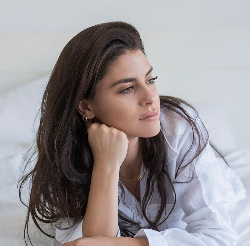 A brunette woman in a white shirt, with her fist slightly pressed under her jaw - PRP Facial in Red Bank, NJ