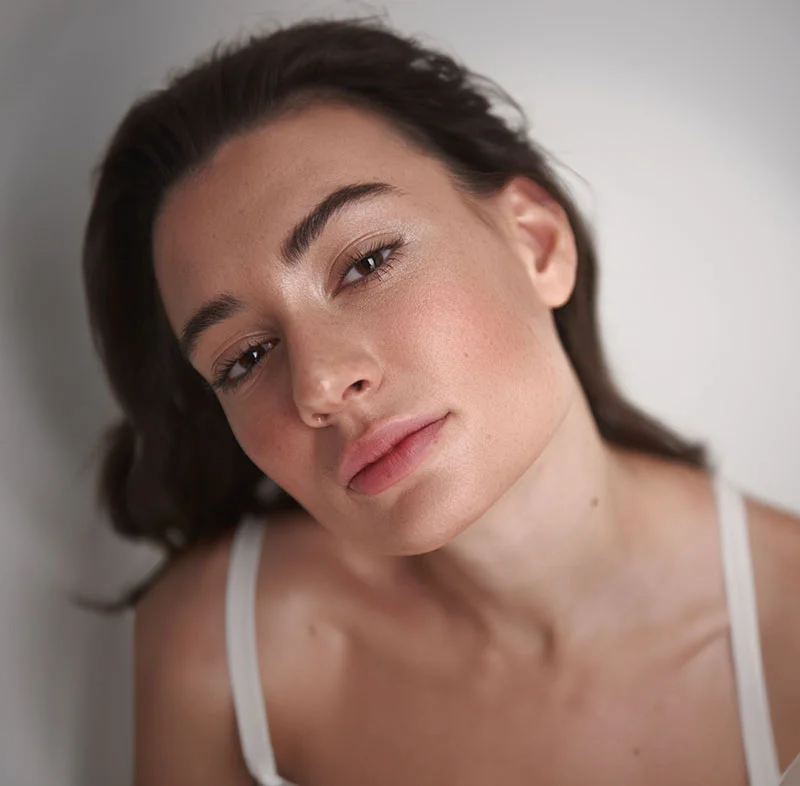 A brunette woman in a white tank top, with her head tilted back - Rosacea Treatment in Red Bank, NJ